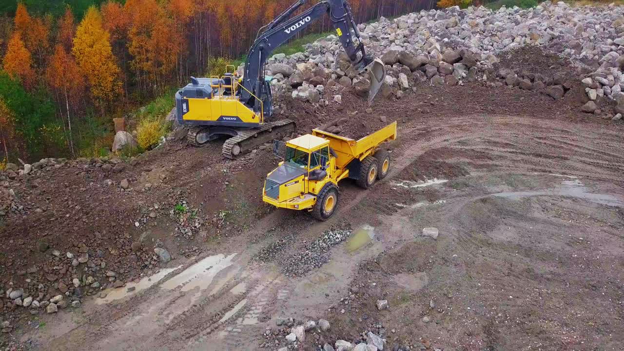 Aerial, orbit, drone shot, around a Crawler Excavators, Volvo EC380EL, filling up Articulated Truck, with soil, in Pohjanmaa, Finland