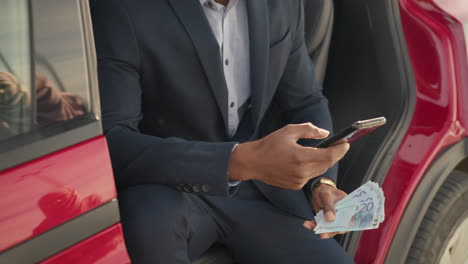 hombre de negocios en un coche eléctrico usando su teléfono inteligente y dinero