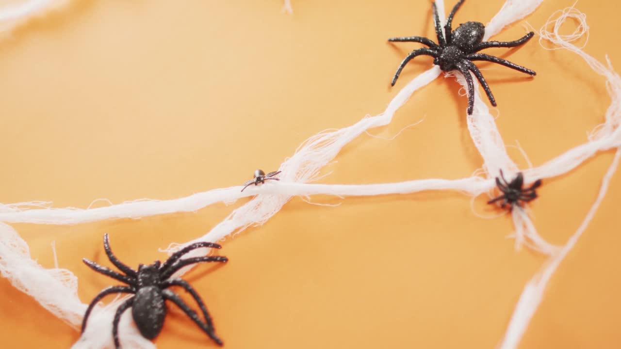 primer plano de varios juguetes de araña que forman una telaraña contra un fondo naranja