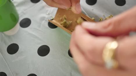 hands crushing up cannabis to make a joint on a picnic table