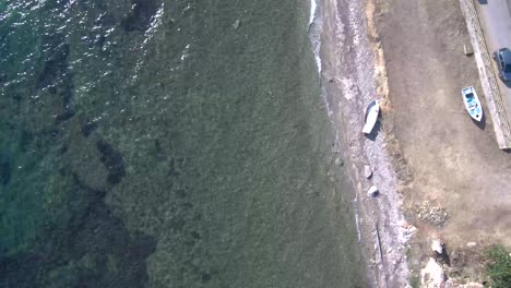 Aerial-view-,-crystal-clear-waters-on-a-Greek-coast-beside-a-road-by-drone