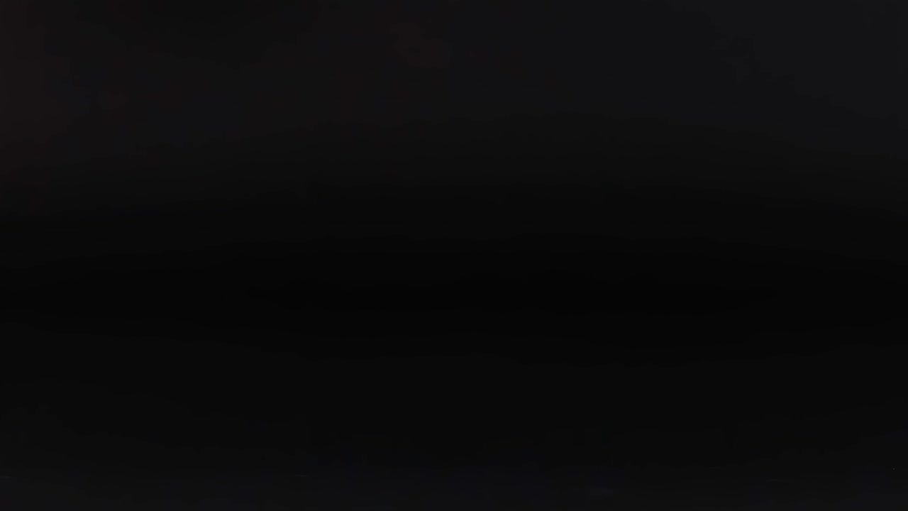 A red cricket ball rolls across a dark surface, showcasing its shiny leather and seam.