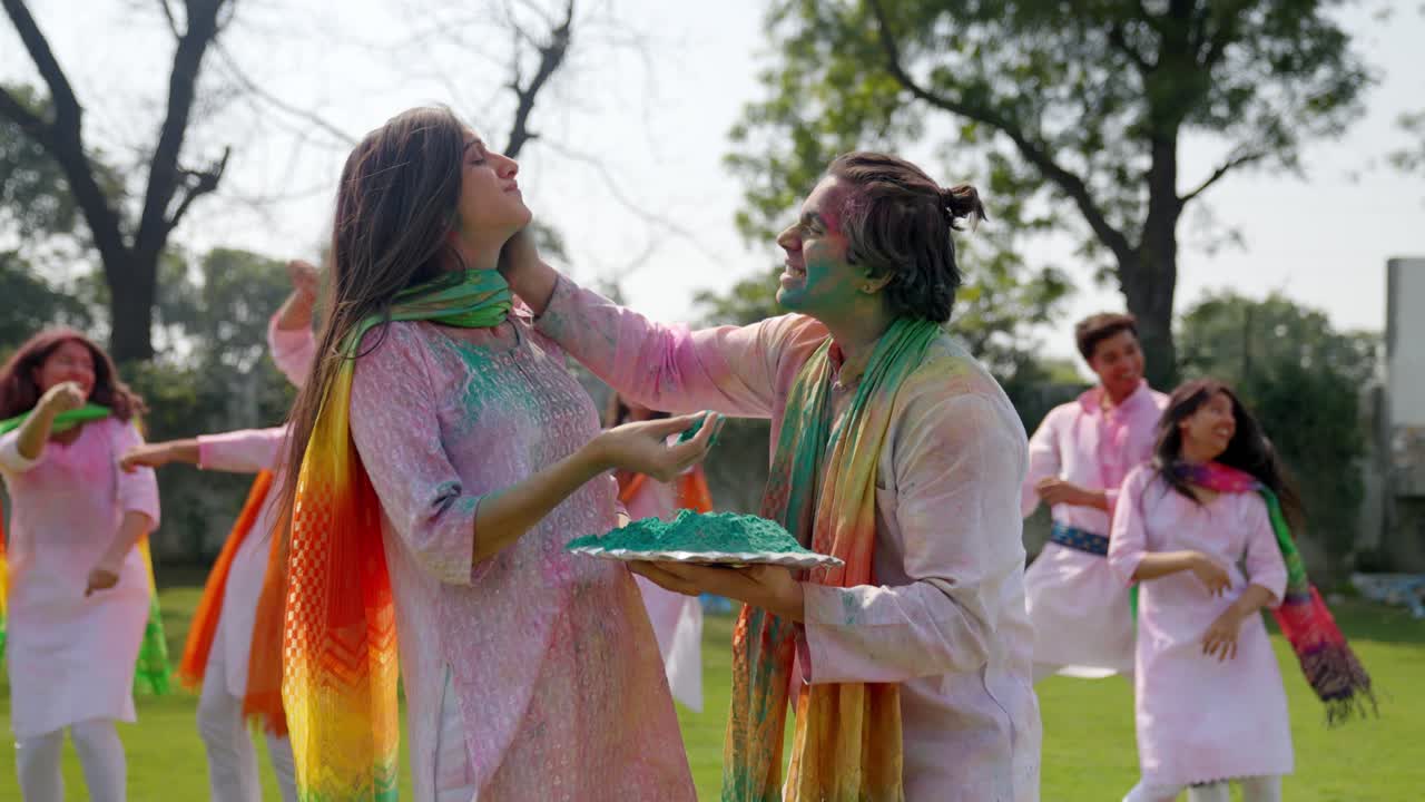 Uomo indiano che applica i colori Holi sul viso della moglie a un festival