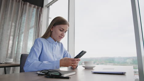 female employee messaging someone on the phone. woman smiles looking at her smartphone. panoramic window at backdrop.