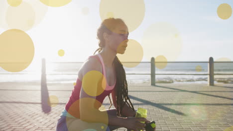 animation of yellow spots over biracial woman drinking water on promenade