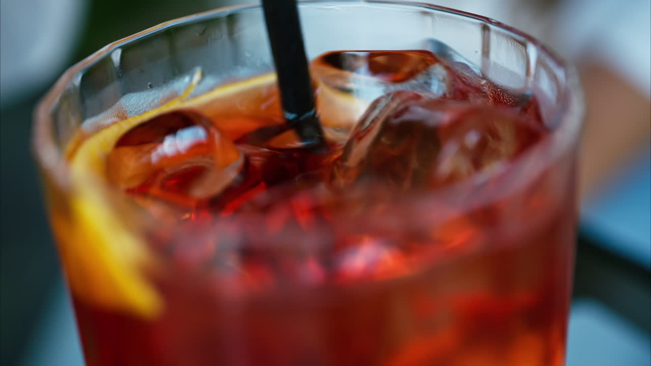 Primo piano di una donna che mescola un cocktail Negroni con una cannuccia