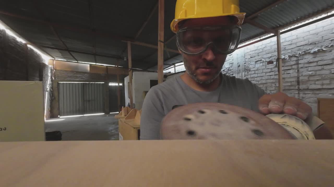 Man in Hard Hat and Goggles Sanding Wood in Workshop