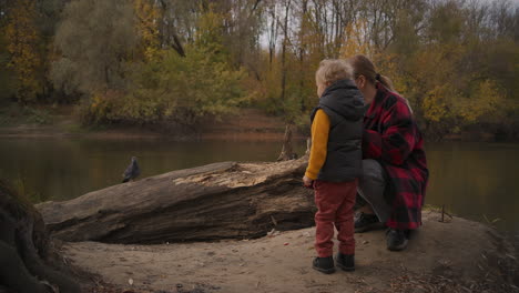 autumn nature in forest little child is exploring mother and boy are playing with dove on shore of lake having fun together resting at weekend