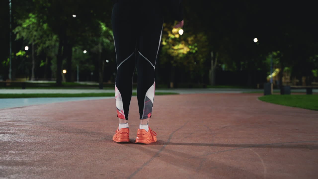 Back View Close Up Of A Fit Girl Stretching Legs And Then Running In The Park At Night