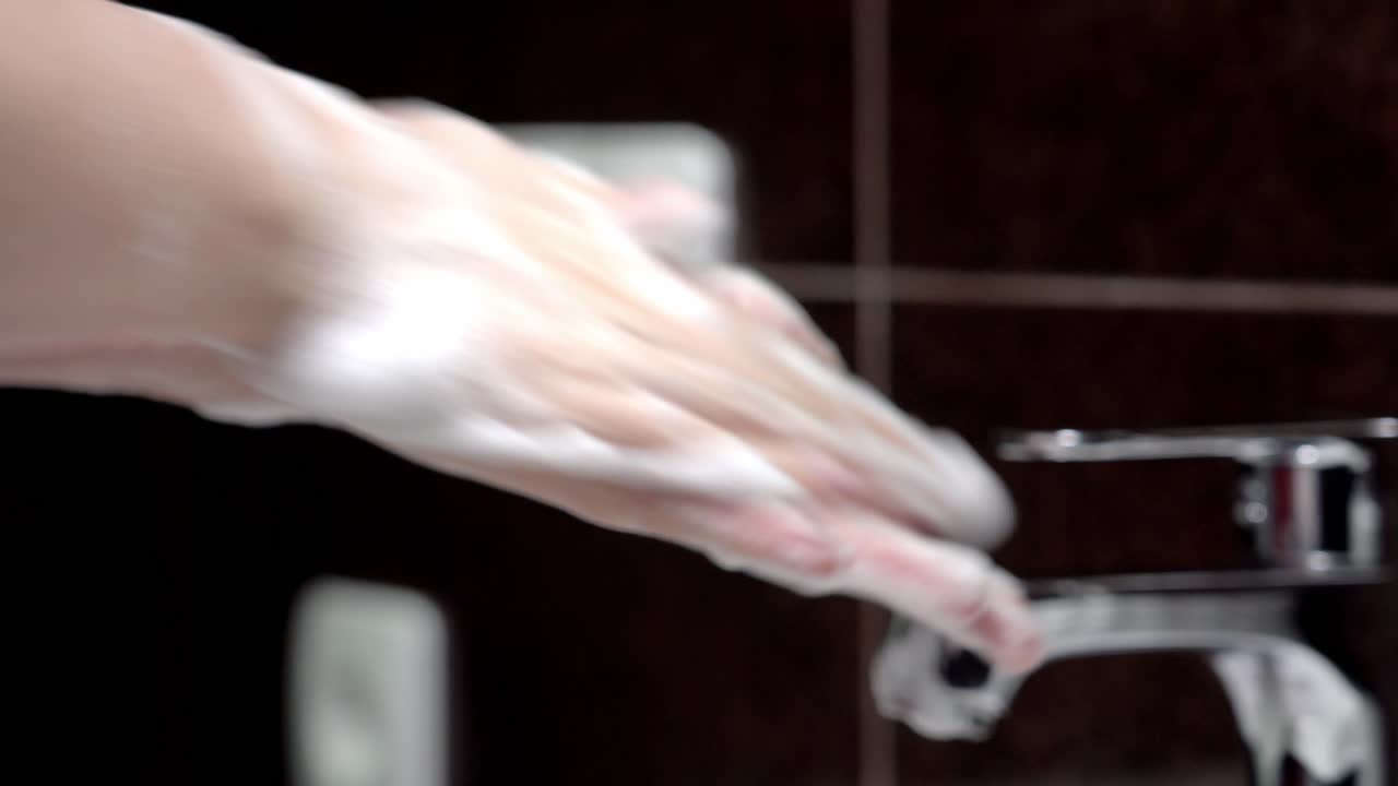 A young girl washes her hands thoroughly with soap.
