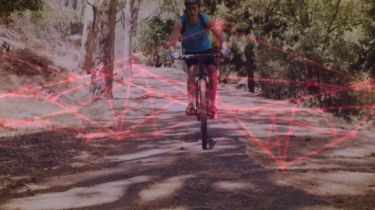 Cyklista vjíždějící a aktivující červenou síťovou technologickou překryvnou grafiku, zatímco se blíží ke kameře a pomalu drží kolo.