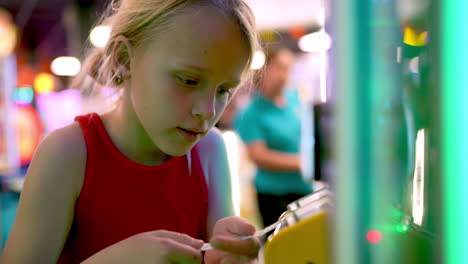 blonde girl in red top inserting arcade tickets into yellow counting machine in game center