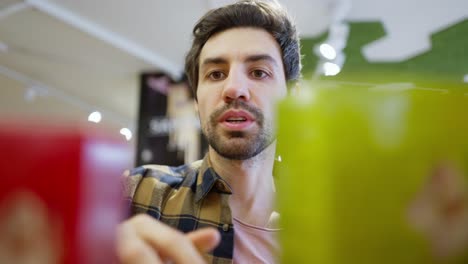 cerca de un hombre moreno confiado con rastro en una camisa a cuadros elige los productos que necesita mientras mira en un estante del supermercado