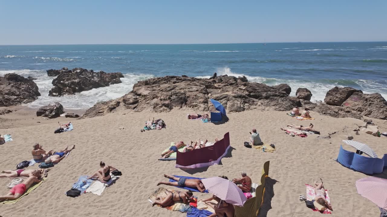 A crowded beach scene at Ingleses Beach in Porto on a sunny day with colorful umbrellas and people