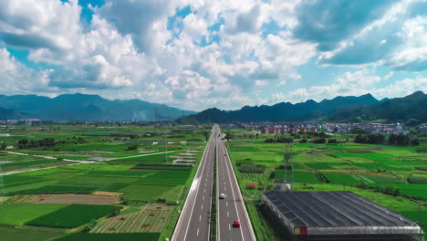 Hermosa-Y-Tranquila-Carretera-Junto-A-Campos-De-Cultivo-Con-Postes-De-Electricidad-Y-Transporte-De-Camiones-De-Carga-Bajo-El-Cielo-Azul-Hacia-Las-Montañas