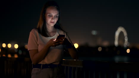 Eine-Junge-Touristin-Reist-Durch-Die-Nächtliche-Großstadt-Und-Schreibt-Textnachrichten-In-Sozialen-Netzwerken-über-Die-Reise,-Hält-Das-Telefon-In-Der-Hand-Und-Schaut-Auf-Den-Bildschirm-Des-Geräts