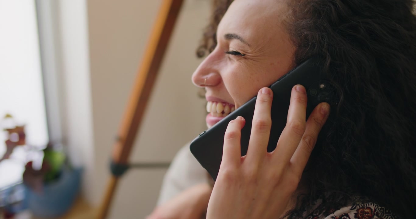 Jovem mulher a falar ao smartphone e a rir em casa.