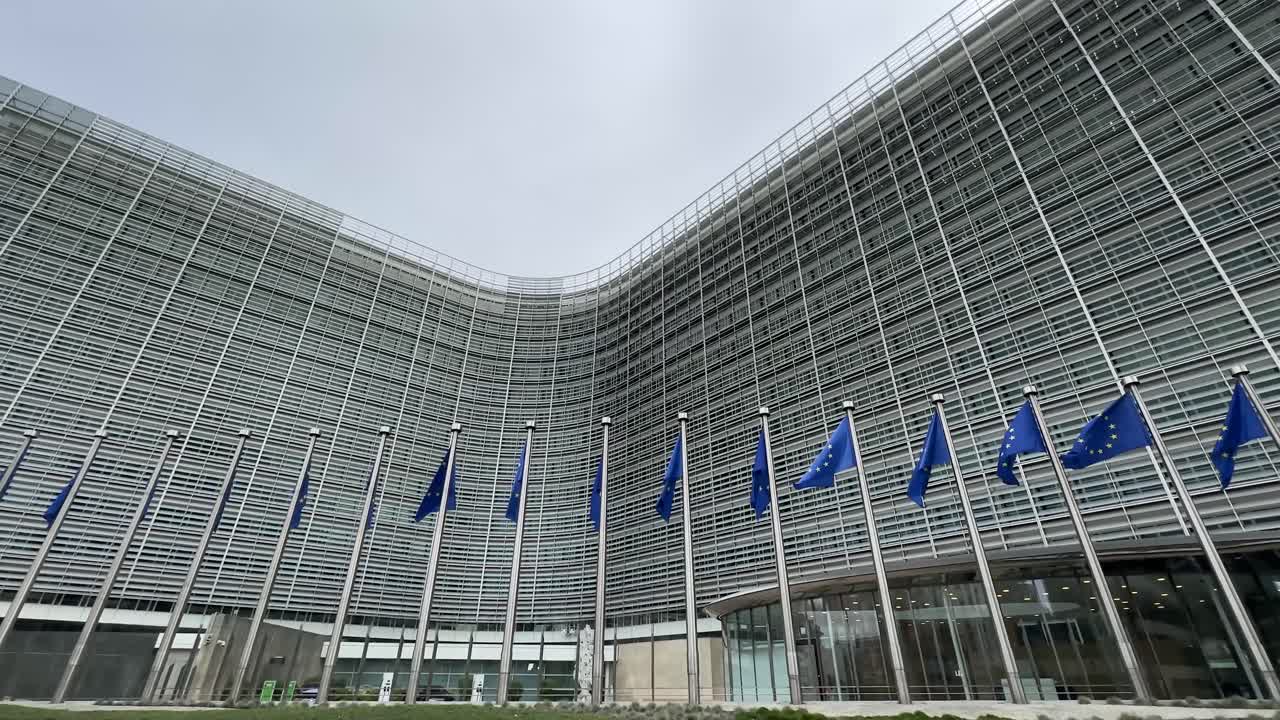 Inquadratura dal basso dell'edificio della Commissione Europea con le bandiere dell'Unione Europea, a simboleggiare politica, governance e istituzioni.
