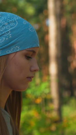 primer plano de hermanas caminando por un bosque iluminado por el sol, una con una mochila roja cubierta de tela, otra con un pañuelo azul, la luz del sol se filtra a través de los árboles, proyectando un suave resplandor en sus rostros