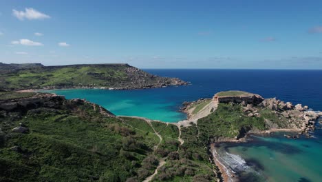 Vista-De-Drones-Sobre-Una-Playa-De-Arena-Tropical-Con-Agua-Turquesa-Clara,-Bahía-De-Gajn-Tuffieha,-Malta