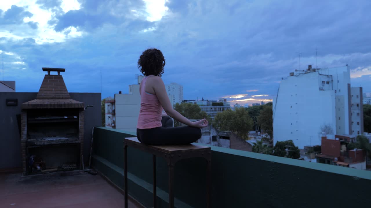 Donna che medita su un tetto con vista sulla città al tramonto