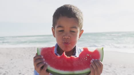 Porträt-Eines-Glücklichen-Hispanischen-Jungen,-Der-Am-Strand-Wassermelone-Isst