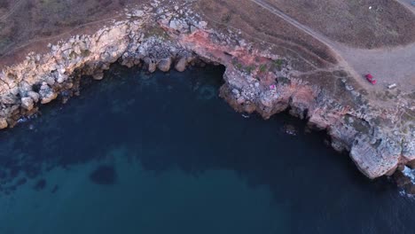 Top-down-aerial-view-of-waves-splash-against-rocky-seashore,-background