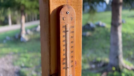 Ein-Hölzernes-Thermometer-Im-Sonnenuntergang,-Berggrüne-Umgebung,-Das-Von-Unten-Nach-Oben-Gleitet