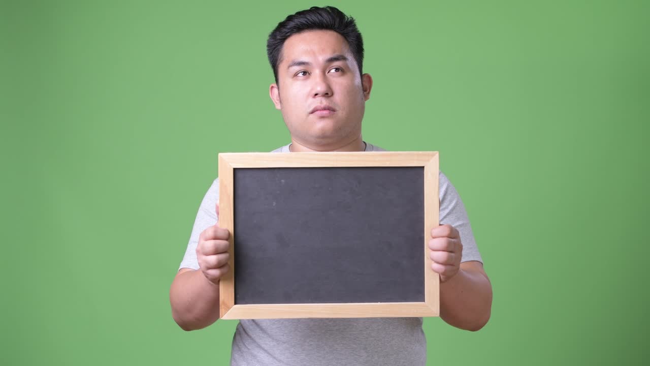 Young handsome overweight Asian man against green background