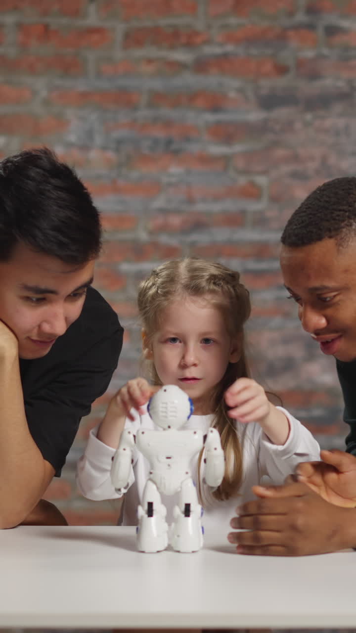 Little girl and black man wave hands to control modern toy robot moves learning engineering with young Asian technician in home classroom