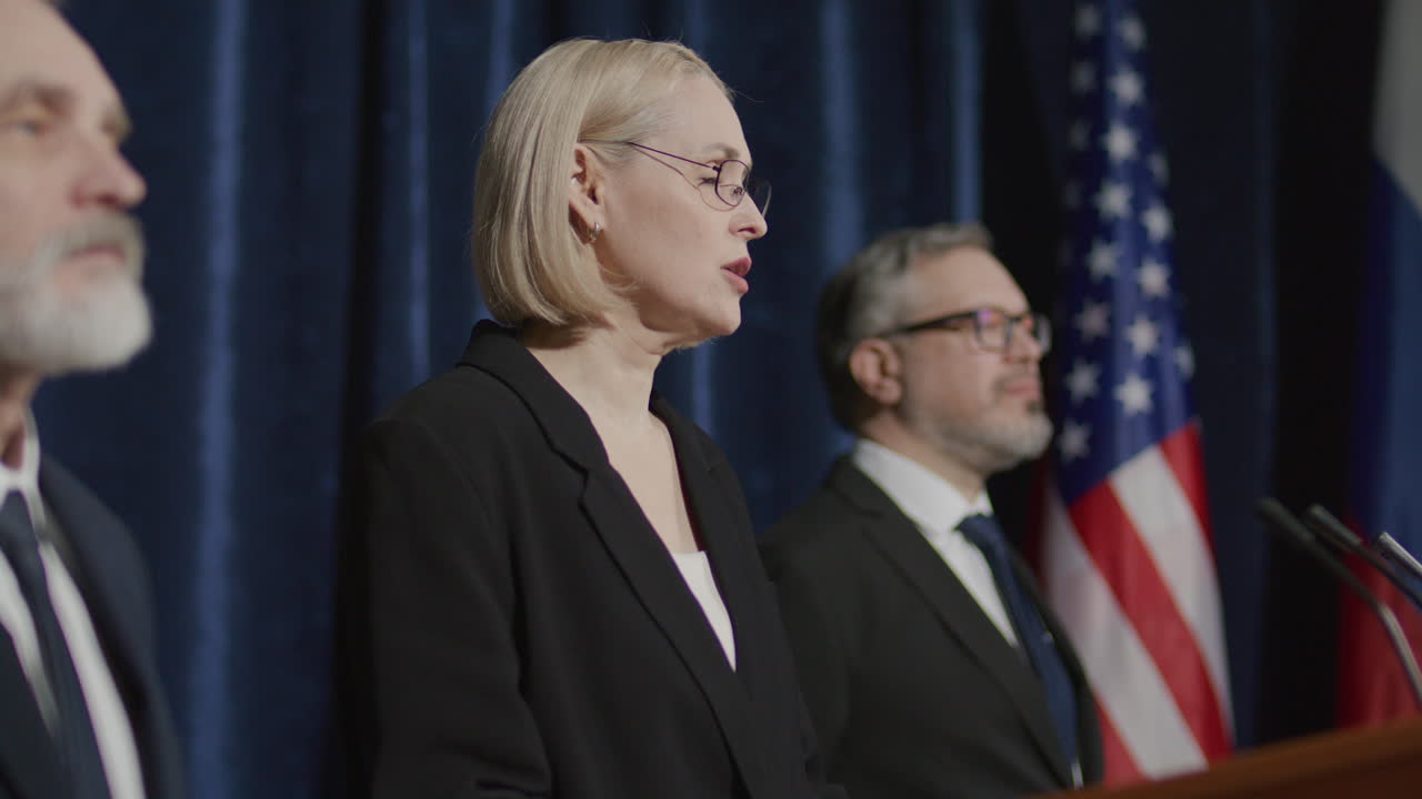 Female Political Leader Standing with Team on Stage, Speaking at Press Event