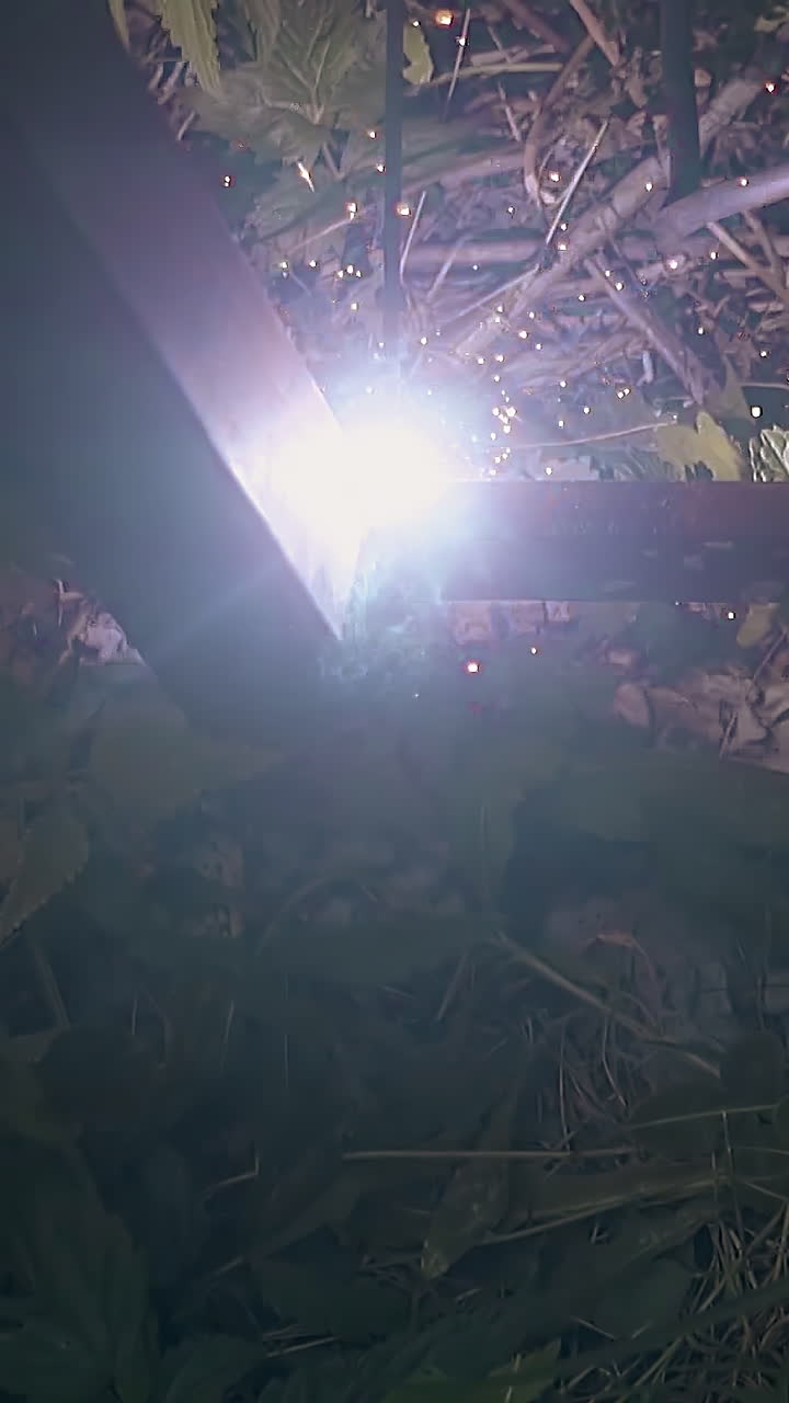 slow motion upper view welding of metal fence carcass bottom parts over ground with green plants
