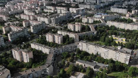 Vista-Aérea-De-Edificios-De-Forma-Geométrica-En-Una-Ciudad-Rodeada-De-árboles-Que-Descienden-Lentamente