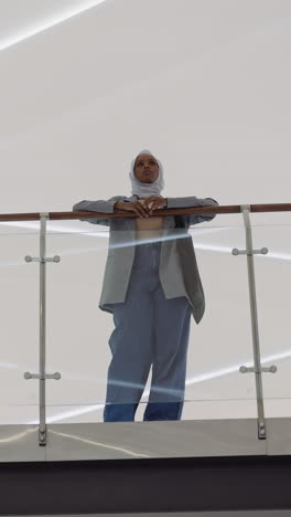 young black woman with hijab leans on glass barrier railing in shopping mall hallway low angle shot slow motion. muslim lady visitor of office center