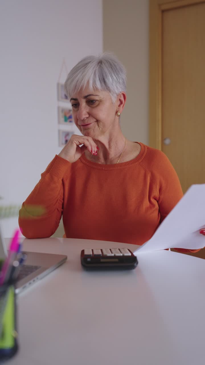 Donna anziana preoccupata che gestisce le finanze domestiche con laptop e calcolatrice