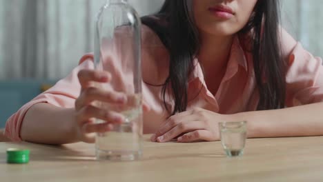 un primer plano de una mujer asiática borracha y deprimida vertiendo vodka en un vaso antes de beber en casa.