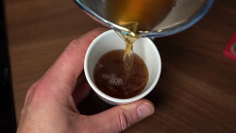 person pouring hot bone broth from pan into mug, slow motion top down view