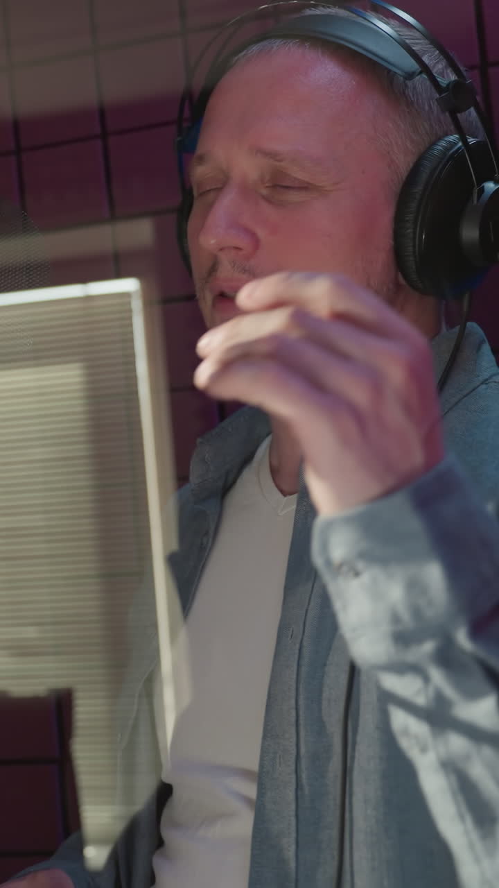 dos hombres en una habitación a prueba de sonido roja cantan con profunda emoción, usando movimientos expresivos de las manos. uno lleva una gorra y camisa negras, mientras que el otro está vestido con una camisa azul y una camisa interior blanca
