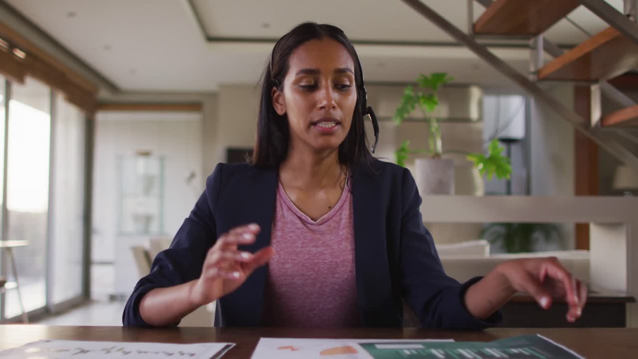 Mixed race woman by desk at home using laptop having video chat