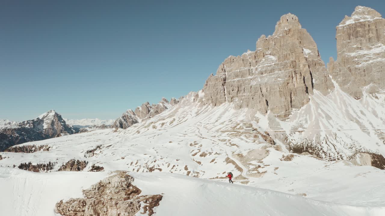 Circling profile drone shot of trekker walking along a steep snowy ridge dolomites tre cime in the background