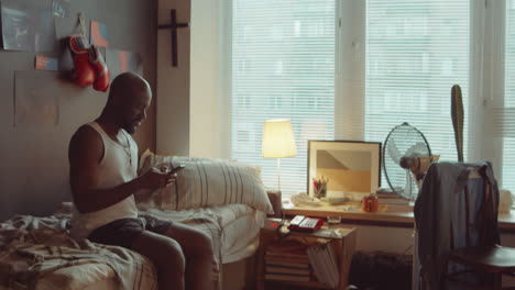 black man sitting on bed and messaging on phone at home