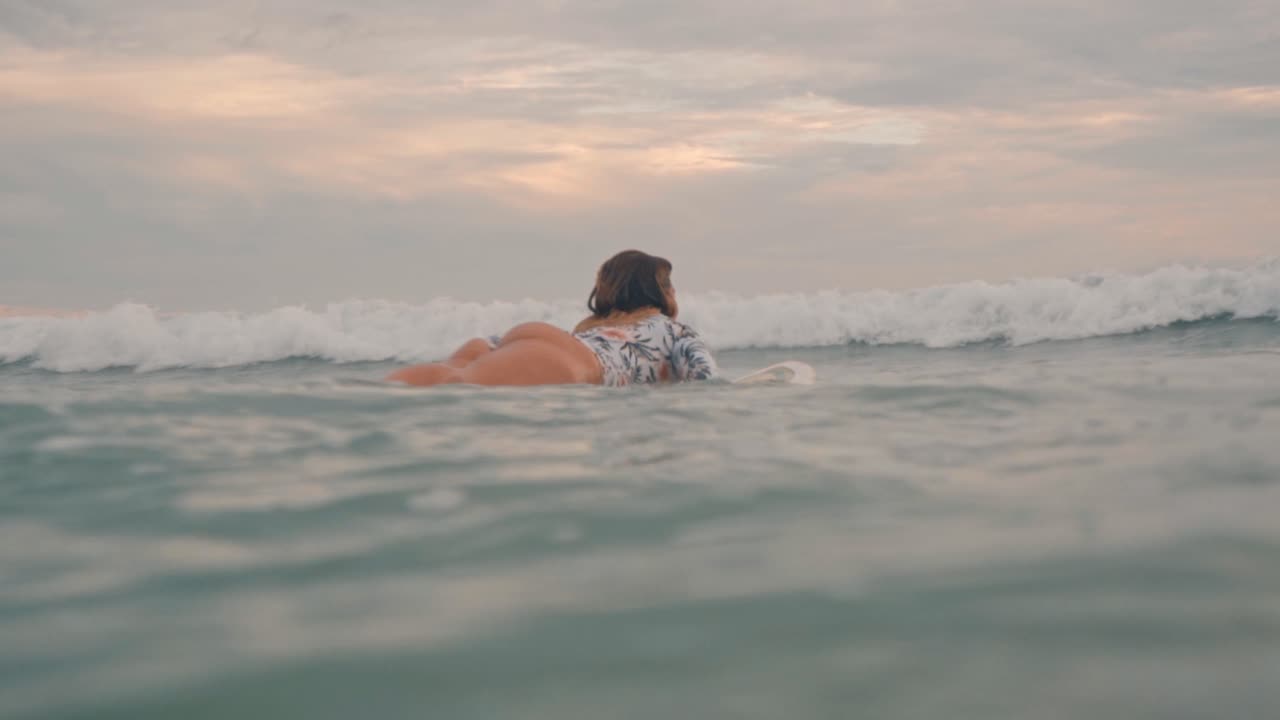 A woman is captured paddling on a surfboard in the calm waters of Santa Teresa, Costa Rica
