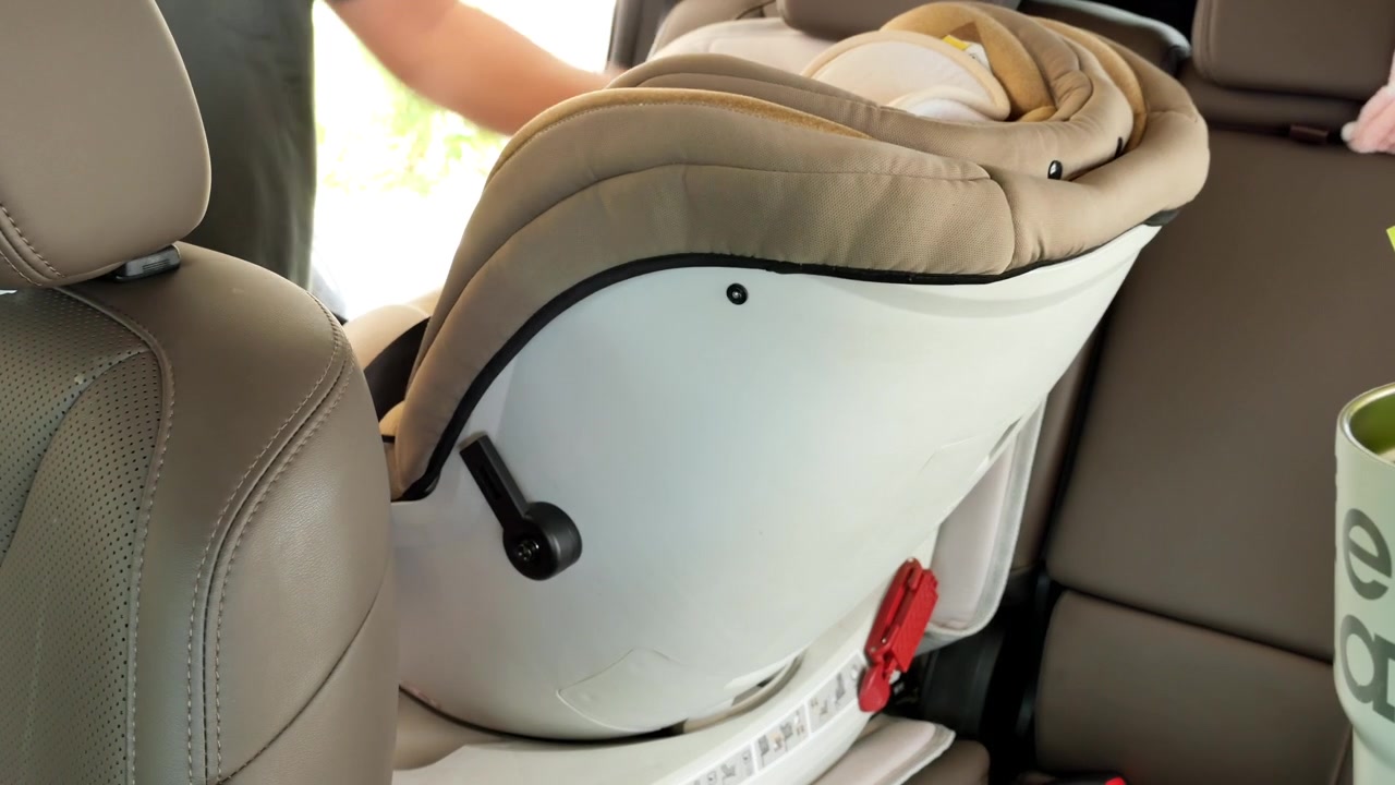 Un hombre ajusta una silla de coche para niños en el asiento trasero de un vehículo, asegurando una colocación segura. Útil para guías de paternidad o tutoriales de seguridad en el coche