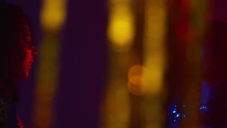 Two-Women-In-Nightclub-Or-Bar-Talking-And-Having-Fun-Shot-Through-Tinsel-Curtain-in-Foreground