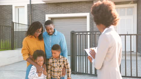 Junge-Afroamerikanische-Familie-Mit-Zwei-Kleinen-Kindern,-Die-Ein-Haus-In-Vororten-Kaufen-Und-Mit-Einer-Immobilienmaklerin-Im-Freien-Sprechen