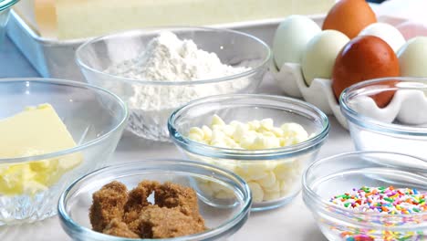 baking confetti sugar cookies and panning across all the cookie ingredients.. in the kitchen making a dessert. making confetti cookies with a white background, pink napkin, chocolate chips and eggs