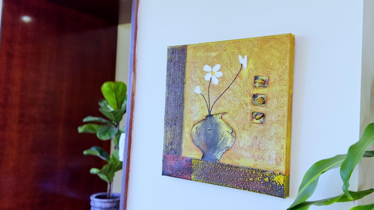 Imagen de decoración interior con estilo de un cuadro amarillo texturizado en pared blanca, acompañado de planta verde. Ideal para decoración del hogar, estilo de vida o visuales de escenificación.