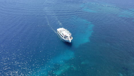 Aerial:-Slow-orbit-shot-of-a-cruise-boat-moving-slowly-on-shallow-turquoise-clear-blue-water