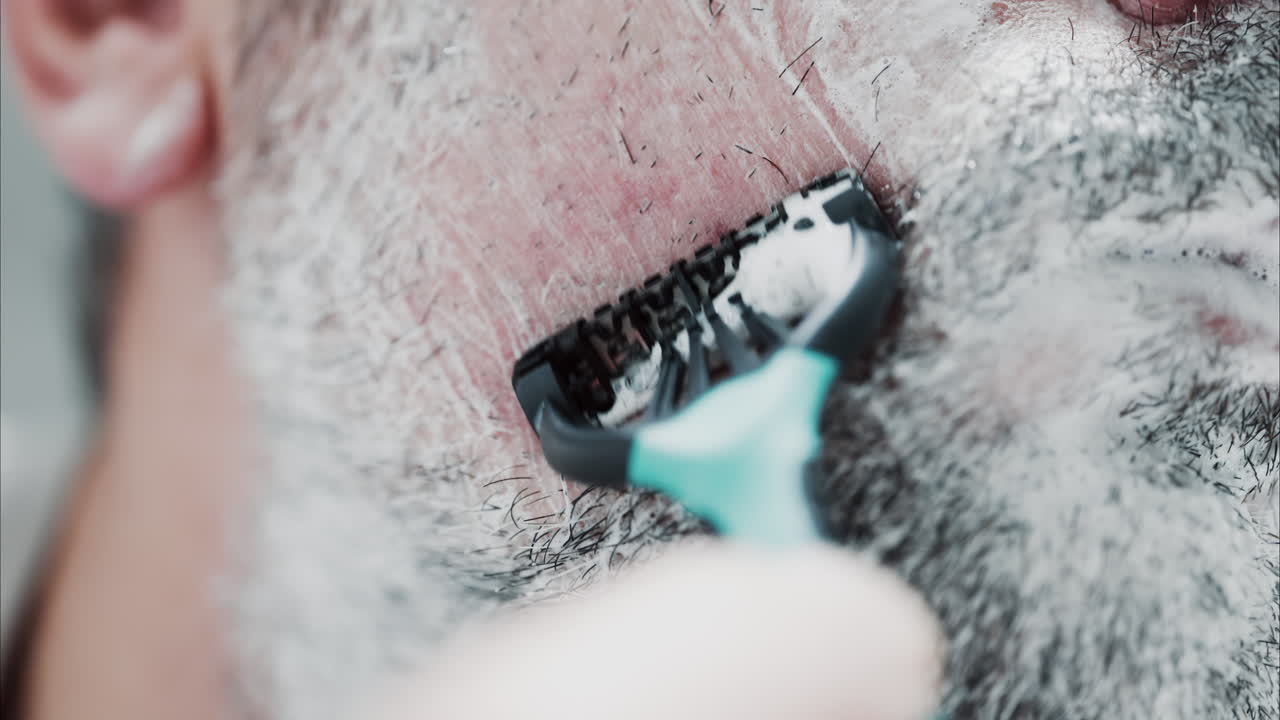 Close up of a man shaving his beard with a razor