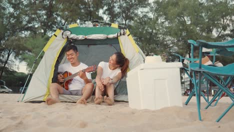 young loving couple pretty while camp playing guitar while sitting at the camping tent on beach